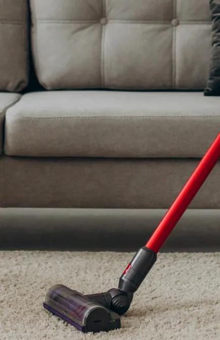 Vacuum cleaner on a cream carpet in front of a grey sofa
